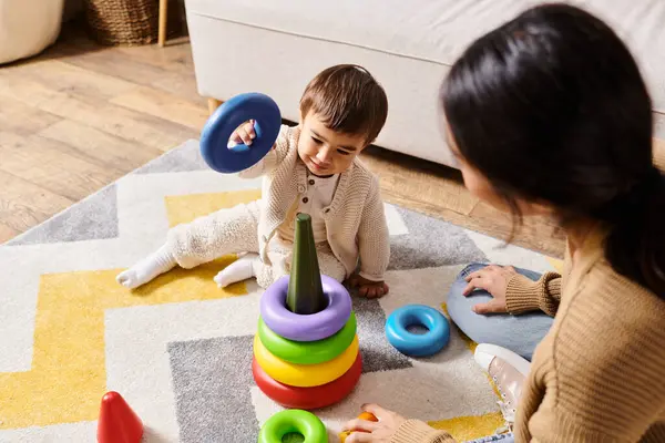 Genç bir Asyalı anne, çocuğuyla oturma odasının zemininde sevgi dolu bir şekilde etkileşime girer..