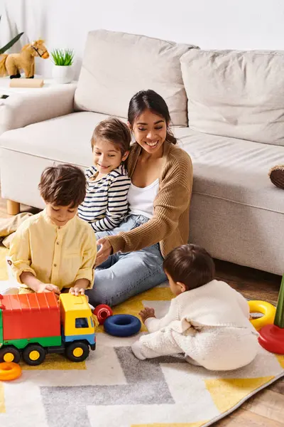stock image A young Asian mother happily sits on the floor, playing with her little sons in the cozy living room at home.