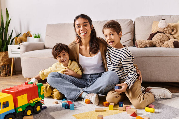 A young Asian mother sits on the floor with her two young sons in their homes living room, engaged in a moment of togetherness and love.