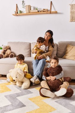 A young Asian mother sits on a couch alongside her little sons in their homes living room. clipart