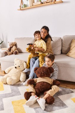 A young Asian mother sits on a couch with her little sons, surrounded by teddy bears, engaged in a cozy cuddle session. clipart