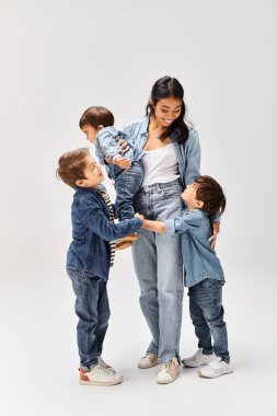 Young Asian mother and her three sons, all dressed in denim, stand united in front of a plain white background. clipart