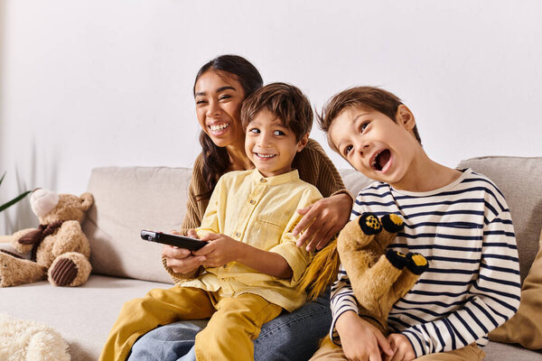 children, along with their Asian mother, relax on a couch holding remote controls in a cozy living room setting.