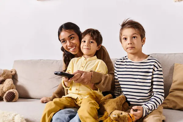 stock image A young Asian mother sits on a cozy couch with her two little sons, creating a heartwarming scene of family togetherness.