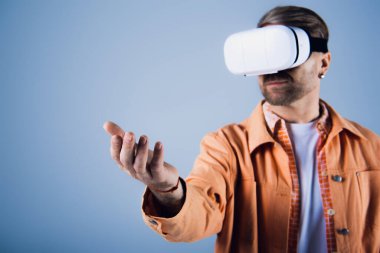 A man in an orange shirt is immersed in the metaverse as he experiences virtual reality in a studio setting. clipart