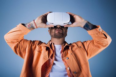 A man in an orange shirt raises a white vr headset above his head in a studio setting. clipart