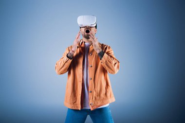 A man in a virtual reality headset explores the digital realm while standing in front of a vibrant blue background. clipart