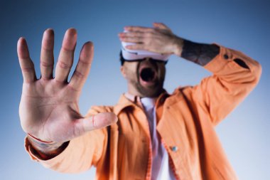 VR kulaklık takmış turuncu gömlekli bir adam stüdyo ortamında çığlık atıyor..