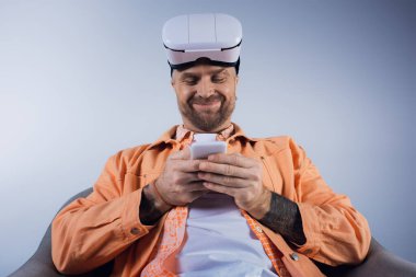 Turuncu gömlekli bir adam cep telefonuna odaklanmış, cihazla etkileşimde..