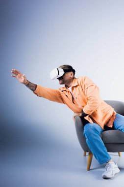 VR kulaklıklı bir adam bir sandalyeye oturur ve elini kaldırır, sanal bir dünyaya daldırır.