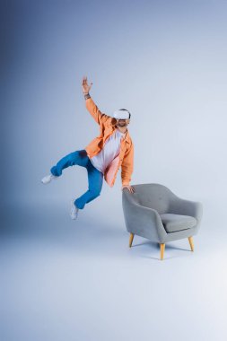 VR kulaklık takan biri stüdyo ortamında bir sandalyenin yanına enerjik bir şekilde atlıyor..
