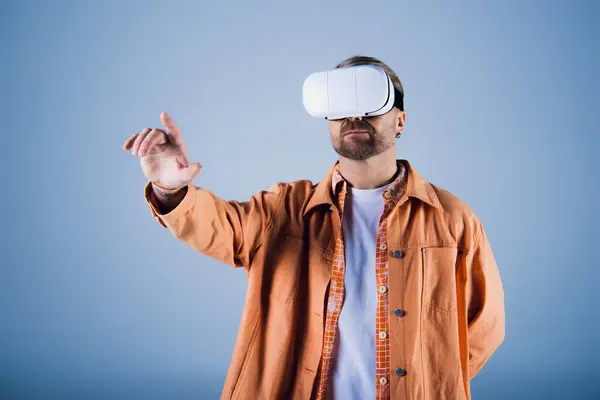 stock image A man in an orange jacket delves into the Metaverse with a virtual reality headset in a studio setting.
