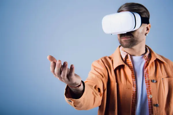 stock image A man in an orange shirt is immersed in the metaverse as he experiences virtual reality in a studio setting.