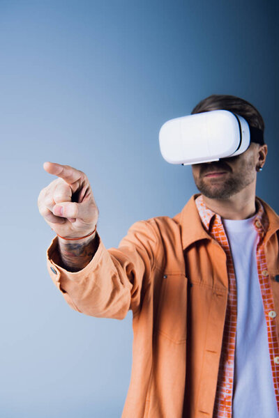 A man in an orange jacket points while wearing a VR headset in a studio setting.
