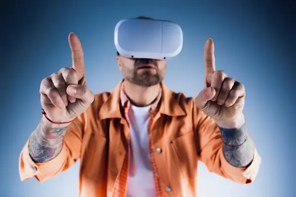 一个穿着橙色衬衫的男人带着一个虚拟现实耳机在工作室里探索数字世界 — 图库照片