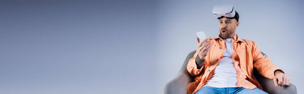 A man in an orange shirt confidently holds a cell phone in his hand.