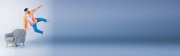 A person wearing a VR headset jumps energetically in the air while balancing on a chair in a studio setting.