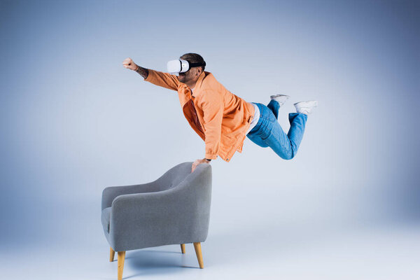 A man in an orange shirt showcasing a gravity-defying trick while balancing on a chair in a studio setting.