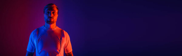 A man in smart glasses stands confidently in a studio, set against a vibrant red and blue background.