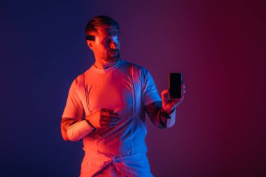 Akıllı gözlüklü bir adam cep telefonunu elinde tutuyor ve etrafındaki sanal gerçeklikle yakından ilgileniyor..