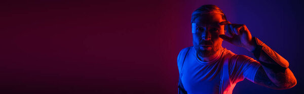 Человек в умных очках уверенно стоит перед ярким красно-синим фоном в студии.