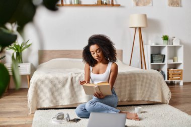 A curly African American woman in a tank top sitting on the floor, engrossed in reading a book in a modern bedroom. clipart