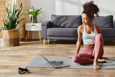 Hareketli kıvırcık Afrikalı Amerikalı kadın rahat bir oturma odasında yoga yapıyor..