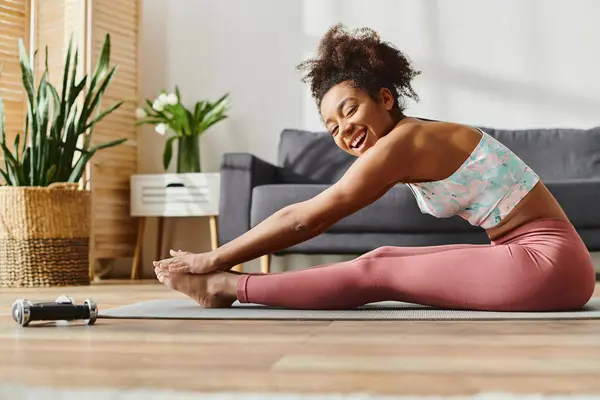 stock image A curly African American woman in activewear is gracefully practicing yoga on the floor at home.