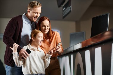 Bir erkek, kadın ve çocuk cep telefonu ekranında toplanmış gülümsüyor ve ailece güzel vakit geçiriyorlar..