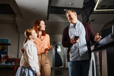 A cheerful family stands close together, enjoying each others company in a cinema. clipart