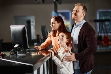 A couple standing in front of a computer with their kid, engrossed in whatever is on the screen, bonding over technology. clipart
