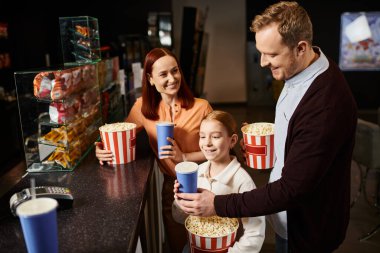 A happy family with a man, a woman, and a child enjoying a movie screening together at the cinema. clipart