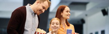 Kadın sinemada patlamış mısır kutusunu tutarken bir adam, karısı ve çocuğunun yanında durup gülümsüyor..