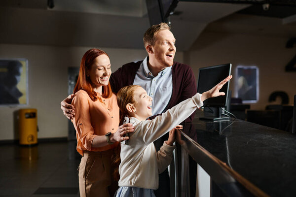 Счастливая семья, мужчина, женщина и ребенок, очарованы чем-то на стене кинотеатра, поглощенным моментом.