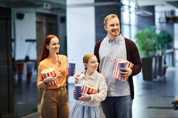 Мужчина, женщина и ребенок счастливо держат попкорн в руках, наслаждаясь фильмом в кинотеатре..