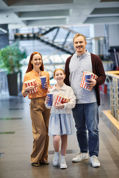 Семья счастливо держит коробки с попкорном, наслаждаясь прогулкой в кино.