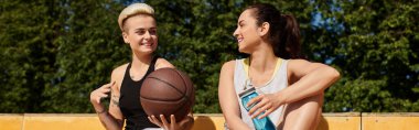 İki atletik genç kadın, güneşli bir günde yan yana oturup, dışarıda basketbol oynuyorlar..