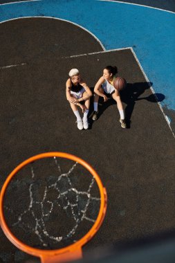 Güneşli bir günde açık hava basketbol sahasının tepesinde oturan bir çift atletik bayan arkadaş..