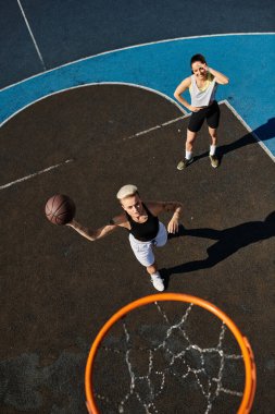 İki atletik kadın basketbol sahasında top sürüyor, ateş ediyor ve güneşin altında heyecan verici bir maçta yarışıyorlar..