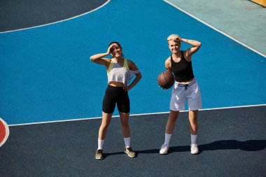 Basketbol sahasının tepesinde gururla duran iki atletik kadın yaz güneşinde güç ve dostluğu simgeliyor..