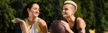 İki genç kadın, arkadaşlar ve sporcular, dışarıda elinde basketbol topuyla durup, spora olan sevgilerini gösteriyorlar..