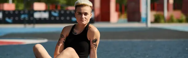 stock image A sporty young woman with short hair and tattoos sits on the ground, legs crossed, contemplating the scenery.