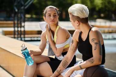 Two young athletic women, friends, sitting together outdoors after playing basketball in the summer. clipart