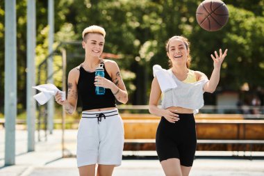 İki genç kadın, arkadaşlar, güneşli bir yaz gününde dışarıda basketbol oynuyorlar..