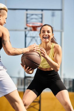 İki genç atletik kadın, biri elinde basketbol topuyla birlikte güneşli bir yaz gününde dışarıda basketbol oynamaya hazırlar..