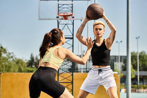 Two young athletic women joyfully compete in a game of basketball outdoors under the summer sun.