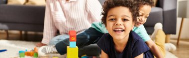 cheerful cute african american boy smiling at camera with his mother and brother on backdrop, banner clipart