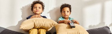 adorable african american boys sitting on sofa with pillows and watching interesting movies clipart