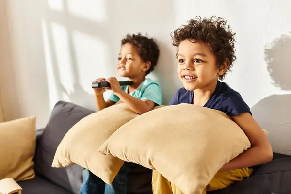 stock image focus on merry african american boy with pillow watching TV next to his blurred adorable brother