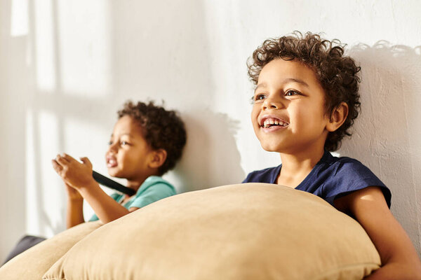 focus on jolly african american boy holding pillow and watching TV next to his blurred cute brother